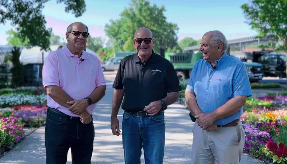 Three men standing in front of a flower garden.