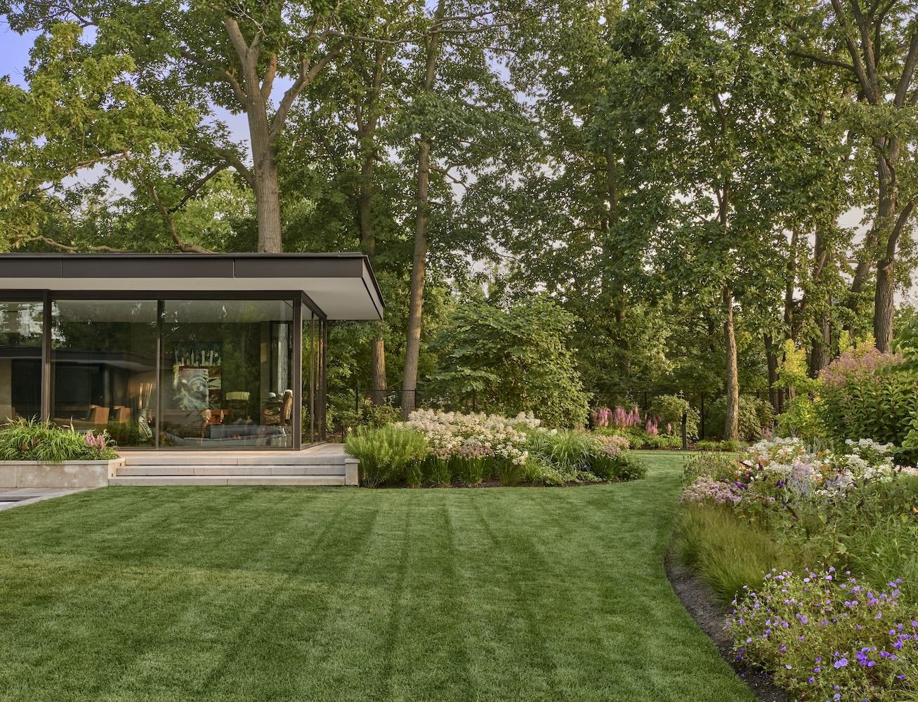 Modern house with large glass walls surrounded by a lush garden and manicured lawn.