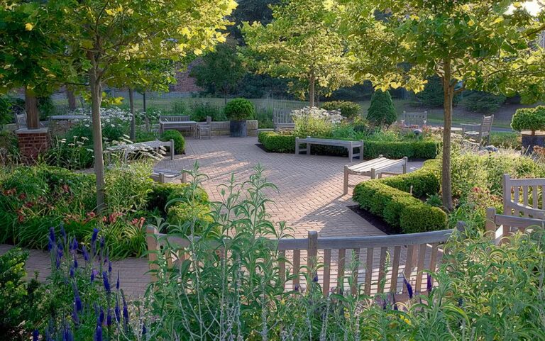 An inviting garden with brick pathways, wooden benches, and lush greenery, lit by soft sunlight filtering through trees.