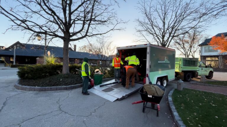 Workers in high-visibility jackets unload equipment from a truck into a residential driveway during twilight.