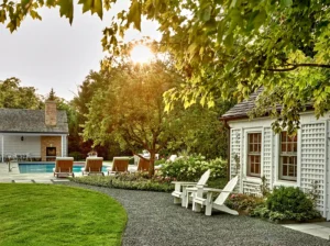 Backyard scene with a pool, lounge chairs, and a small house. Lush greenery surrounds the area, with sunlight filtering through the trees.
