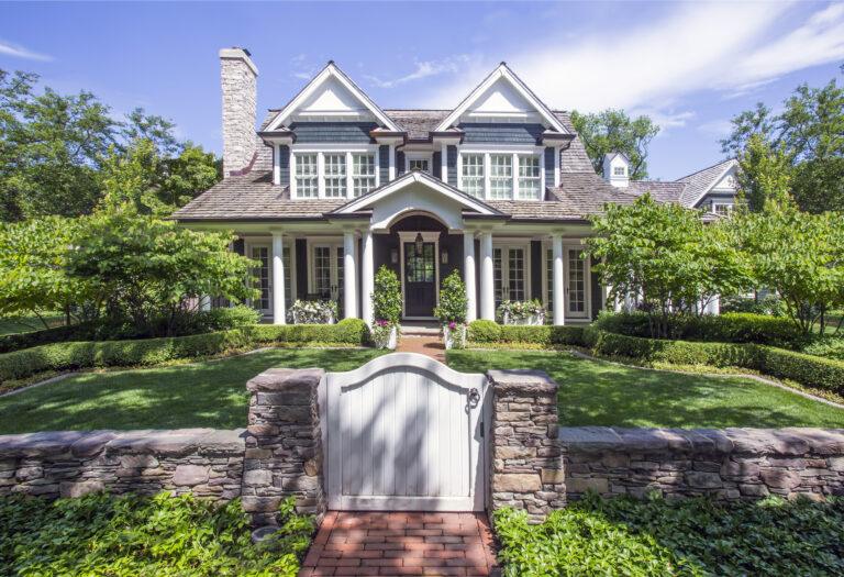 A two-story house with multiple gables in IL, surrounded by manicured landscaping in Hinsdale, viewed from a brick path and stone gate in the foreground.
