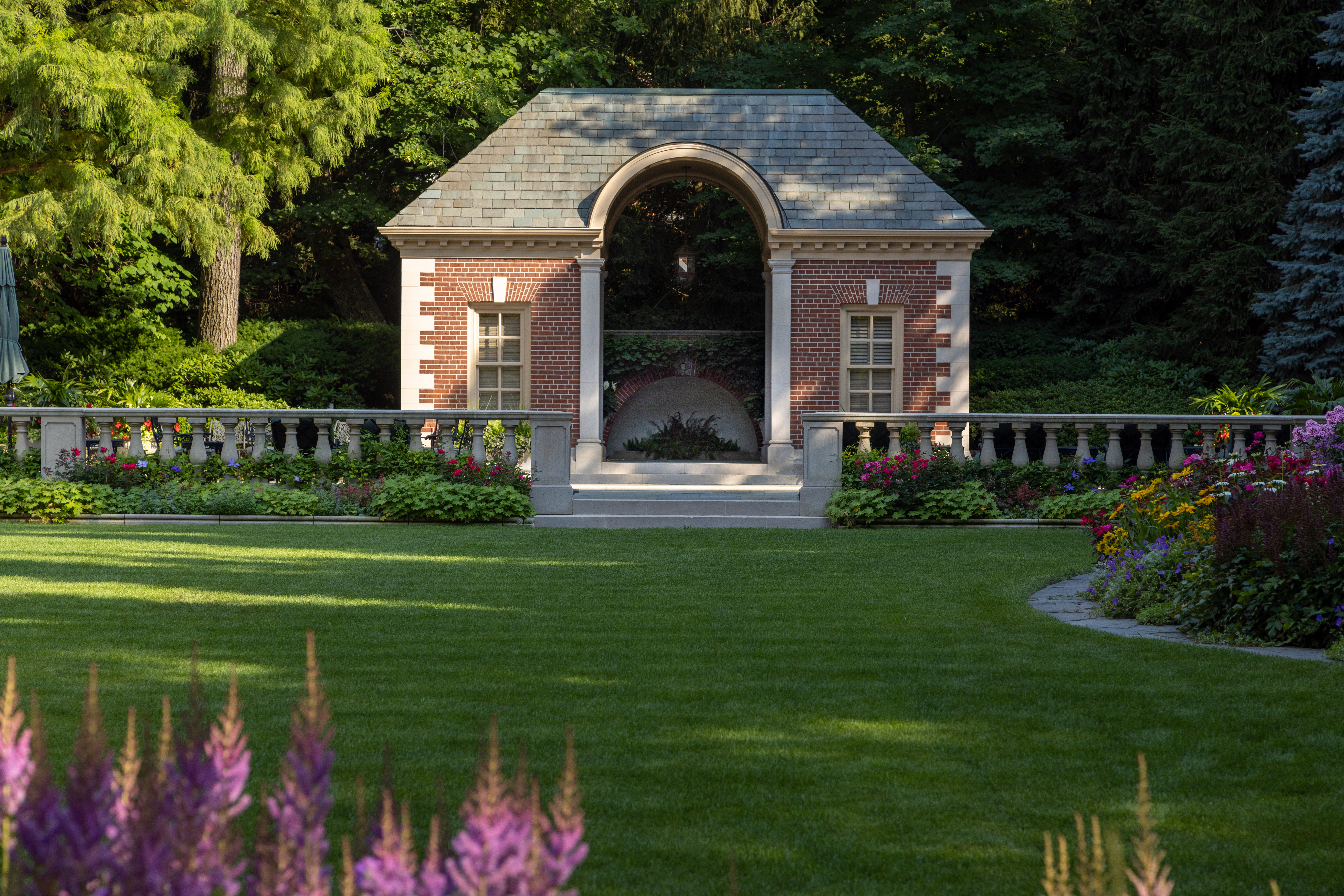 Formal estate garden with brick pavilion, manicured lawn, and flowering borders